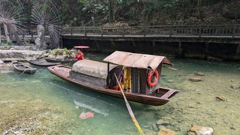       A traditional boat on clear water, bordered by a bridge.
  