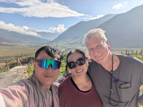 Three people posing with a scenic valley and mountains in the background.