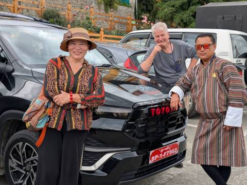       Three people posing next to a car with Bhutanese attire.
  