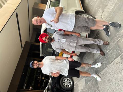 Three men standing in front of a car, one in a traditional turban