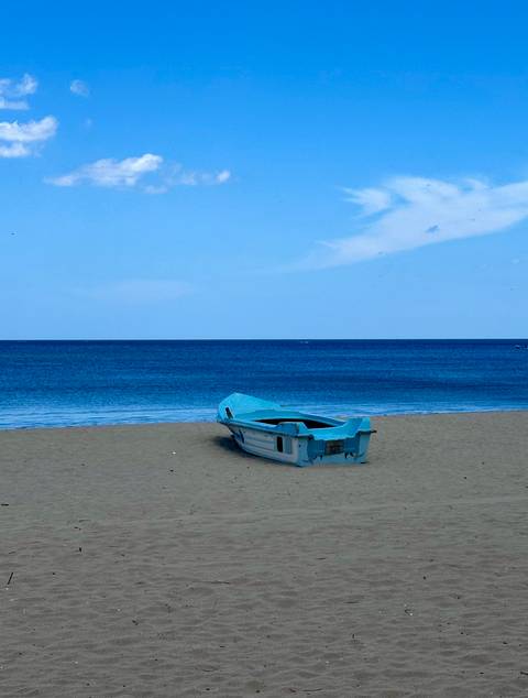 Empty blue boat on a sandy beach by the ocean