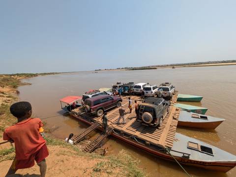       Vehicles on a river ferry with people enjoying the journey.
  