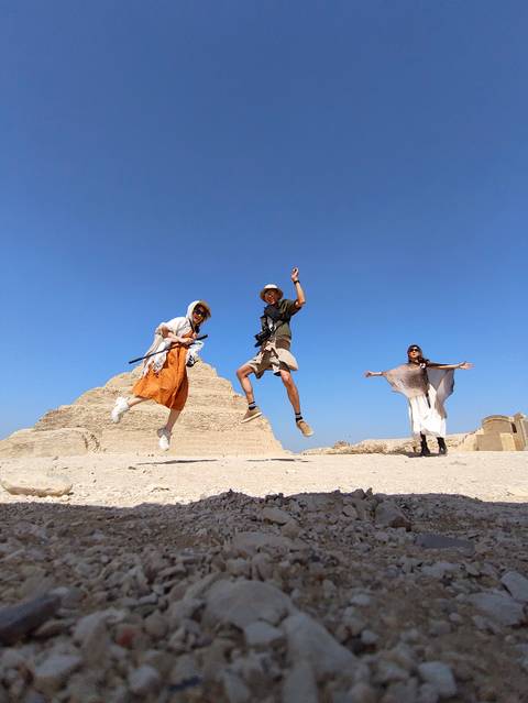 Group jumping in front of a pyramid under a clear blue sky.