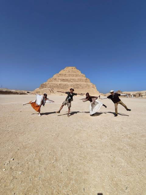 Four people posing in front of a pyramid on a sunny day.