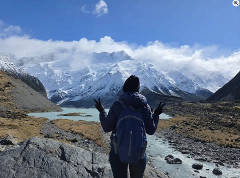       Person with arms outstretched facing snow-capped mountains.
  