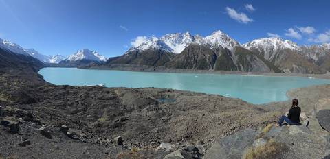       Person sitting by a turquoise lake surrounded by mountains.
  