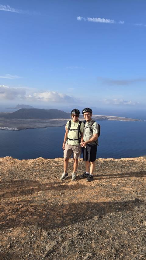       Two people posing on a cliff with ocean and island view.
  