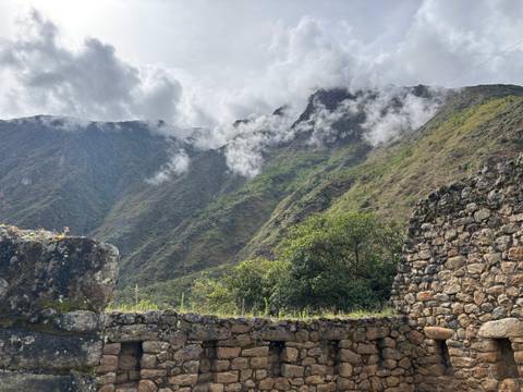 Cloud-kissed mountains with ancient stone walls in the foreground.