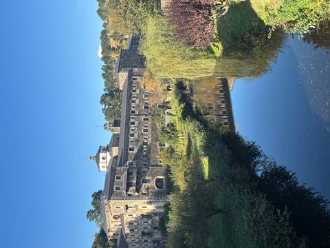 Historic building by a river in a lush area.