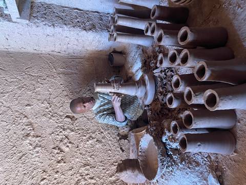       Man working with clay pots in a traditional setting.
  