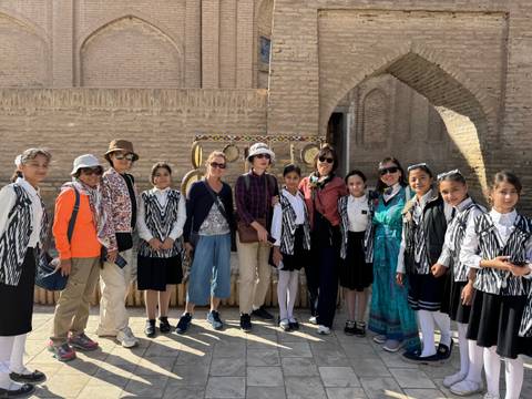 Group of people and local children in traditional attire standing in front of a historic structure.