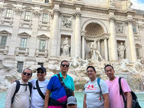 Group of men posing in front of the Trevi Fountain.