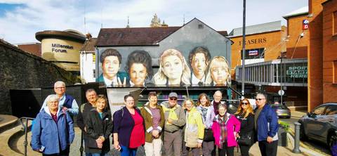       Group of tourists posing in front of a building with murals.
  