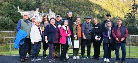       Tourists posing in front of a historic castle surrounded by greenery.
  