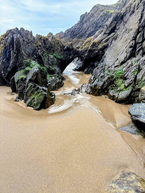      Sandy beach path through rocky cliffs leading to the ocean.
  