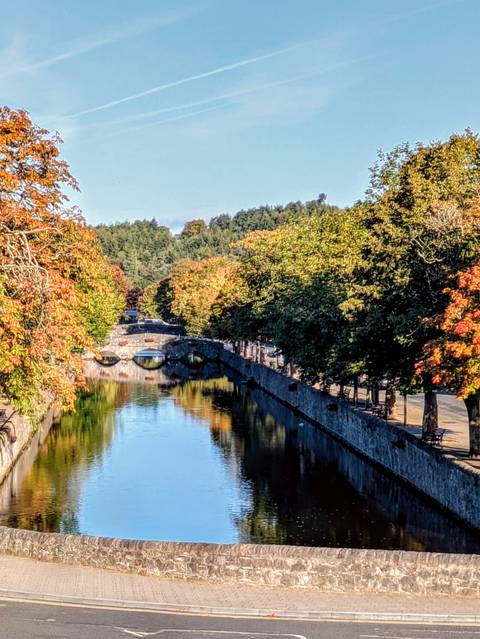       A calm river with arched stone bridges surrounded by autumn trees.
  