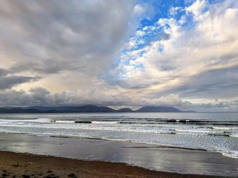       A scenic view of a beach with mountains in the distance under a partly cloudy sky.
  
