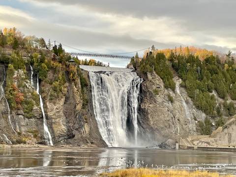 Waterfall cascading down rocky cliffs with a suspension bridge above.