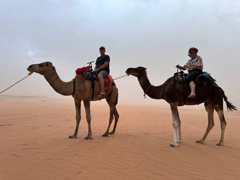       Two people riding camels in a sandy desert.
  