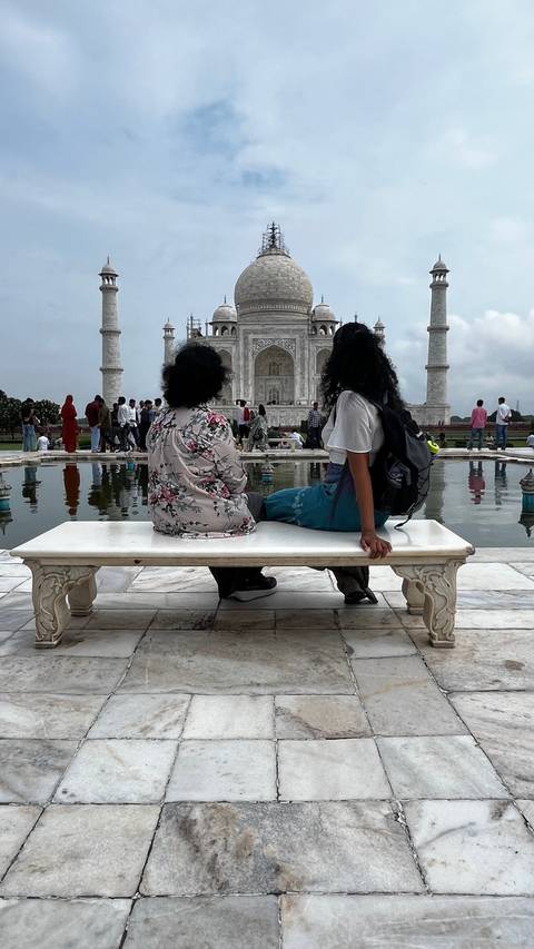       Two people sitting on a bench with the Taj Mahal visible in the background.
  