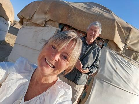 Two people smiling in front of a yurt in a desert-like setting.