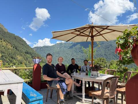 Group of people sitting under an umbrella with a mountain view.