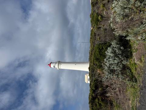       Lighthouse under a cloudy sky on a coastal hill.
  