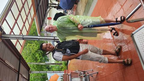 Two men standing together on a rainy day, one in a rain poncho.