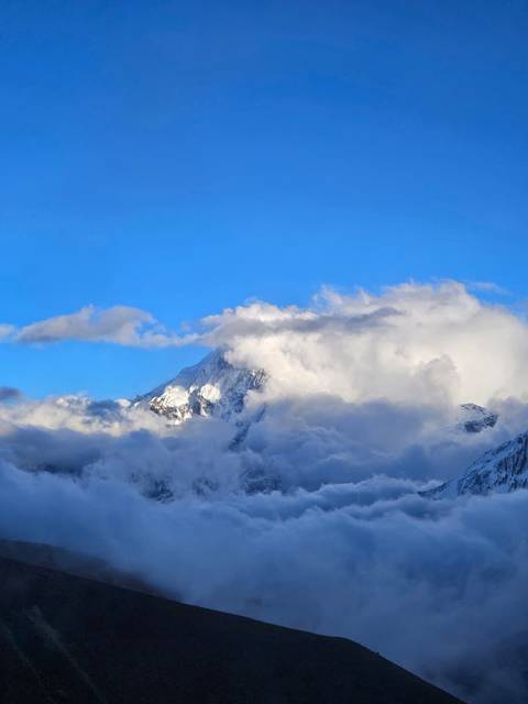       Snowy mountain peak partially obscured by clouds.
  