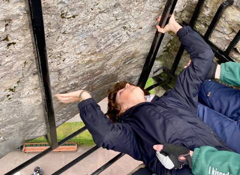 Person leaning backward at Blarney Castle, holding onto a railing.