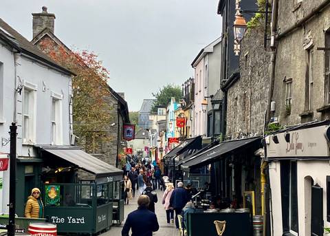       Busy street scene in a historic town with many people walking.
  