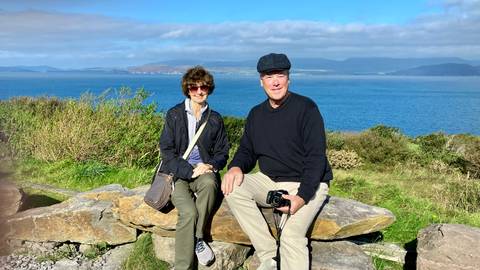 Couple sitting on a rock with a scenic view of the ocean and mountains.