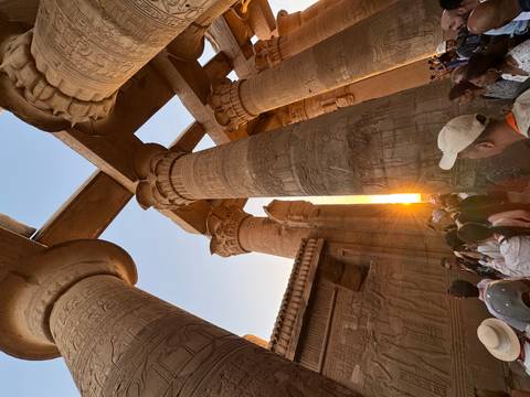 Tourists exploring an ancient temple with hieroglyphs at sunset.