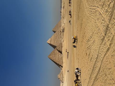       Pyramids of Giza with tourists and camels in the foreground.
  