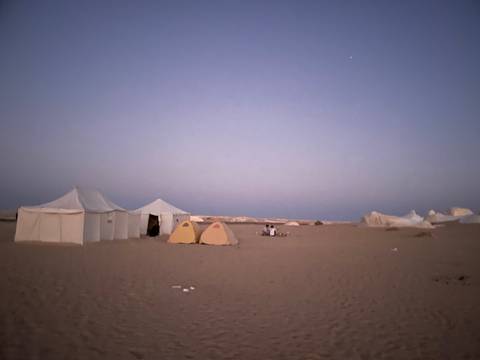       Camping tents at dusk in a desert setting.
  