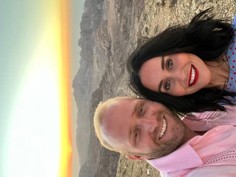 Couple taking a selfie with a desert landscape at sunset.