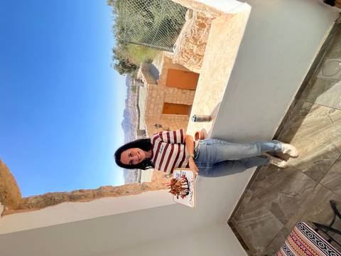 Woman holding a cake with a scenic desert view from a balcony.