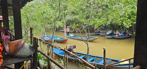       People using traditional boats on a narrow river surrounded by greenery.
  