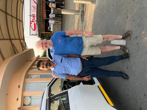 Two men standing together next to a vehicle.