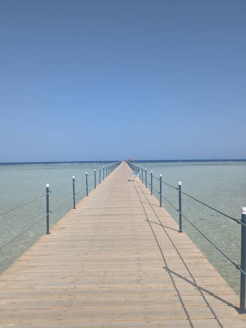 Long boardwalk leading into an expansive ocean view, with a clear sky.