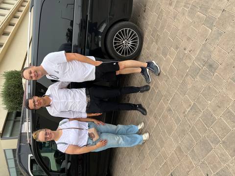 Three people standing together in front of a vehicle.