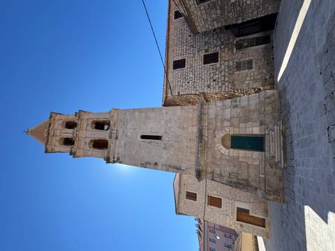       Tall bell tower in a stone courtyard under a clear blue sky.
  
