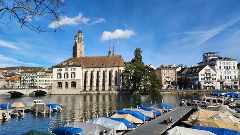 A river with boats and historic buildings in the background, with clear blue sky.