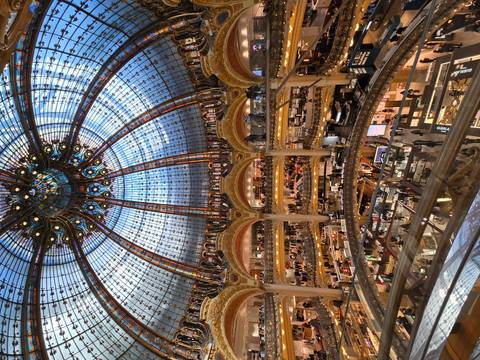 Interior of a grand building with an ornate glass dome and shops.