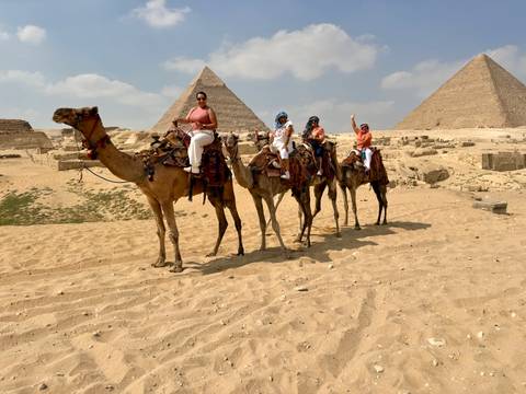 People riding camels with pyramids in the background.