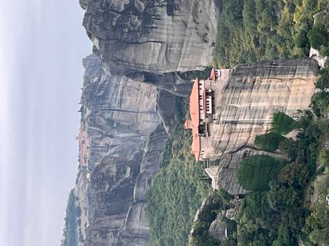       Monastery on a rock cliff with greenery around.
  