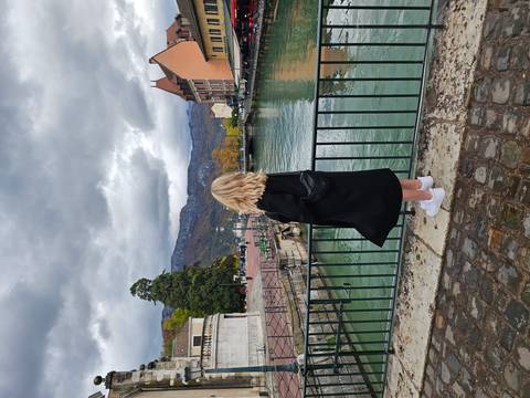       Person standing by a river with historical buildings in the background.
  