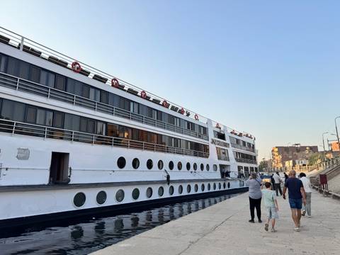 People walking along a dock next to a large river cruise ship.
