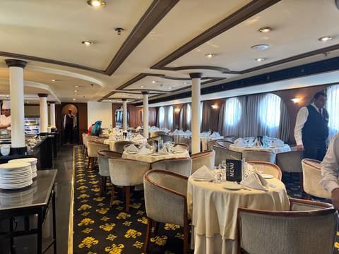 Elegantly set tables in a ship's restaurant with servers.