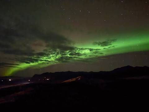 Northern lights over mountains and a dark landscape.